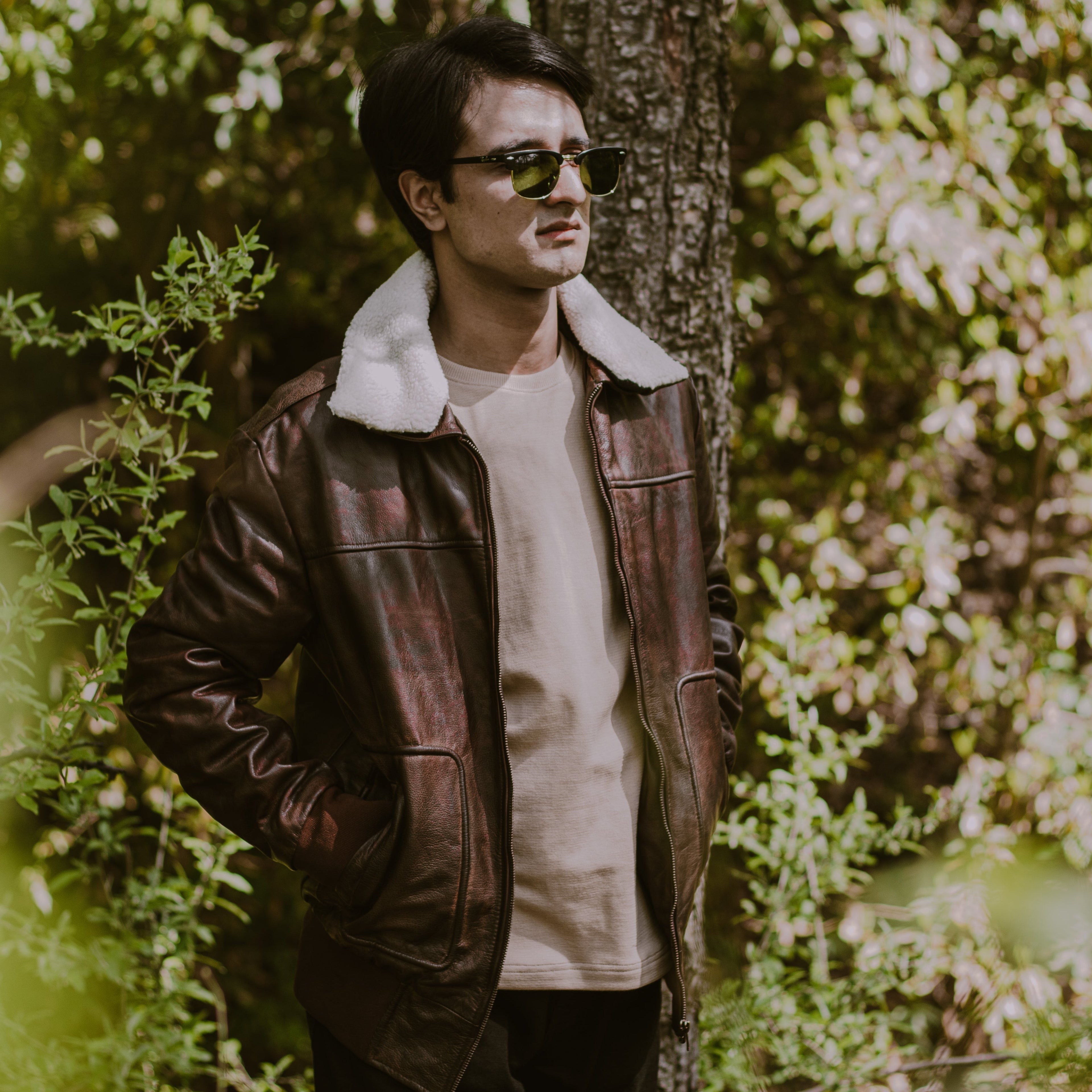Man wearing a leather jacket and sunglasses standing in a forest