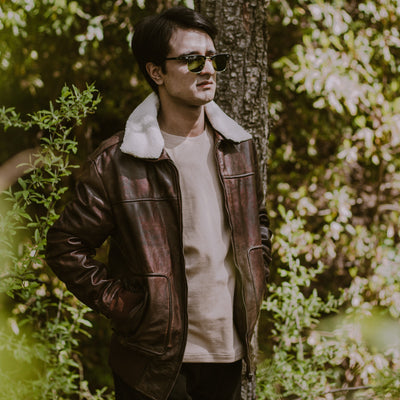 Man wearing a leather jacket and sunglasses standing in a forest