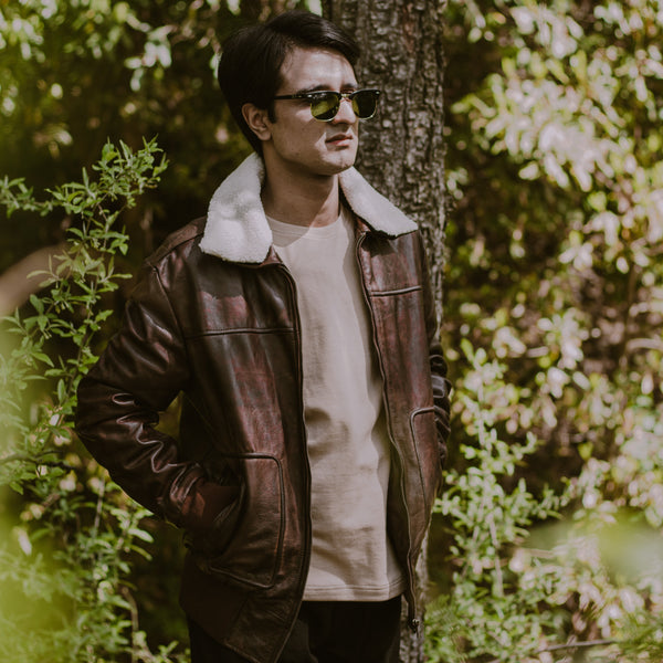 Man wearing a leather jacket and sunglasses standing in a forest