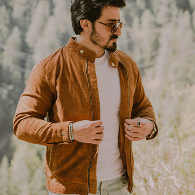 Man wearing a brown suede racer jacket and sunglasses in a natural setting