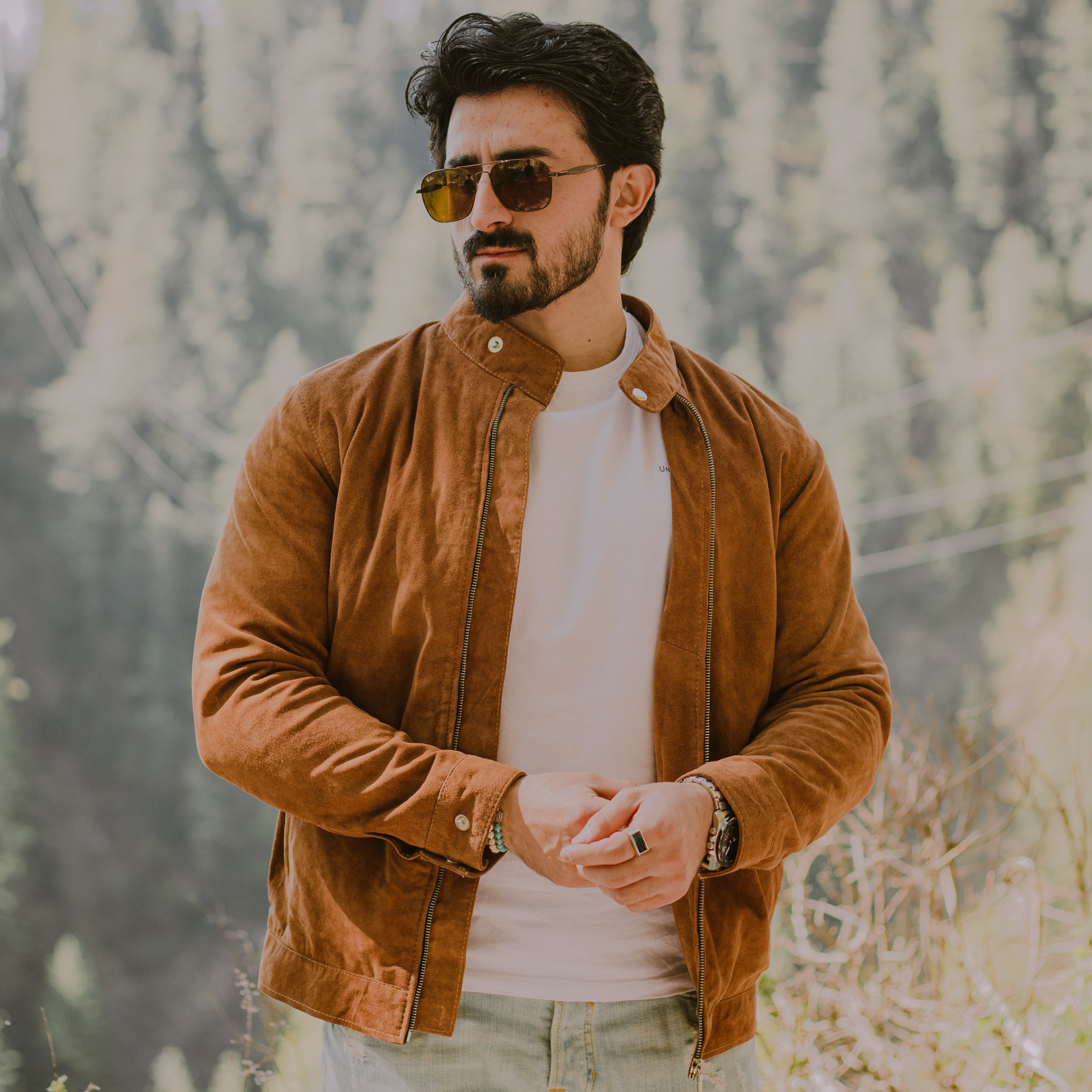 Man wearing a brown suede racer jacket and sunglasses with a blurred natural background