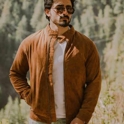 Man wearing a brown suede racer jacket and sunglasses with a forest background