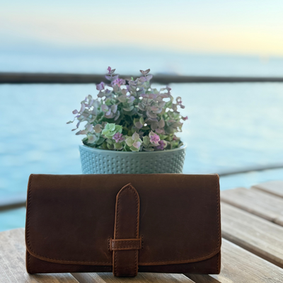 Brown leather clutch on a wooden table with a blurred outdoor background