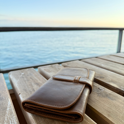 Brown leather wallet on a wooden surface with water in the background